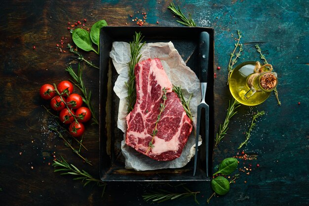 Bifteck de faux-filet de boeuf cru sur l'os avec du thym, du romarin et des épices Vue de dessus Vue de dessus à plat sur la table de coupe en pierre noire