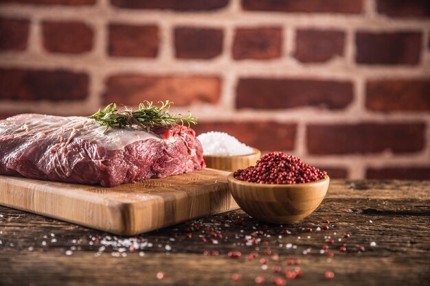 Bifteck de faux-filet de boeuf cru avec sel, poivre et herbes sur planche de boucher en bois.