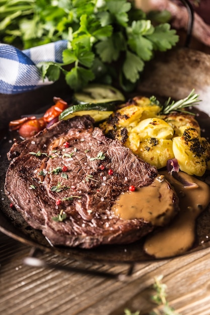 Bifteck de faux-filet de boeuf juteux pommes de terre rôties avec sauce légumes grillés sel poivre et herbes dans une poêle vintage.