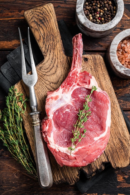 Bifteck de faux-filet cru non cuit ou steak de bœuf (veau) Tomahawk sur une planche à découper de boucher. Fond en bois. Vue de dessus.