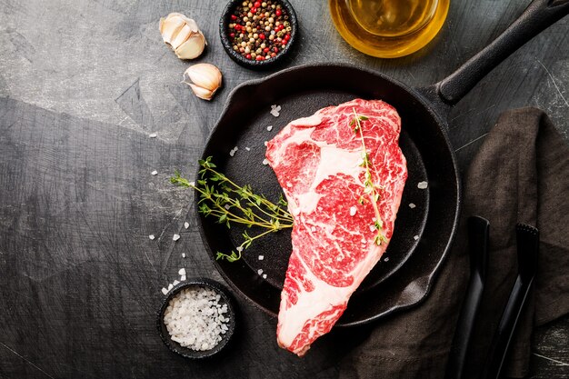 Bifteck de faux-filet frais cru, viande de bœuf avec assaisonnement et casserole de cuisson à l'obscurité