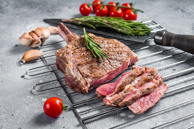 Bifteck de faux-filet tranché rôti au barbecue Tomahawk sur le gril. Fond gris. Vue de dessus.