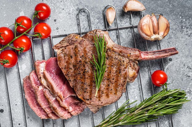 Bifteck de faux-filet tranché rôti au barbecue Tomahawk sur le gril. Fond gris. Vue de dessus.