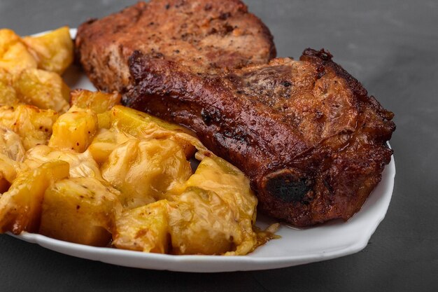 Bifteck de longe de porc et pommes de terre au four avec du fromage sur une assiette blanche