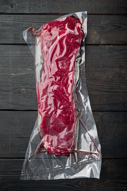 Bifteck de surlonge dans un emballage sous vide. Ensemble de pack de marché, sur fond de table en bois noir, vue de dessus à plat