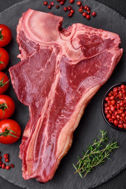 Bifteck de tbone de boeuf juteux frais cru avec du sel, des épices et des herbes sur un fond de béton foncé