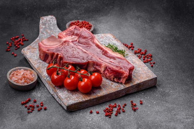 Bifteck de tbone de boeuf juteux frais cru avec du sel, des épices et des herbes sur un fond de béton foncé