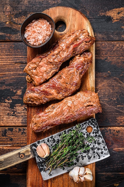Biftecks de jupe marinés crus en sauce barbecue sur une planche à découper en bois avec des herbes sur table en bois. Vue de dessus.