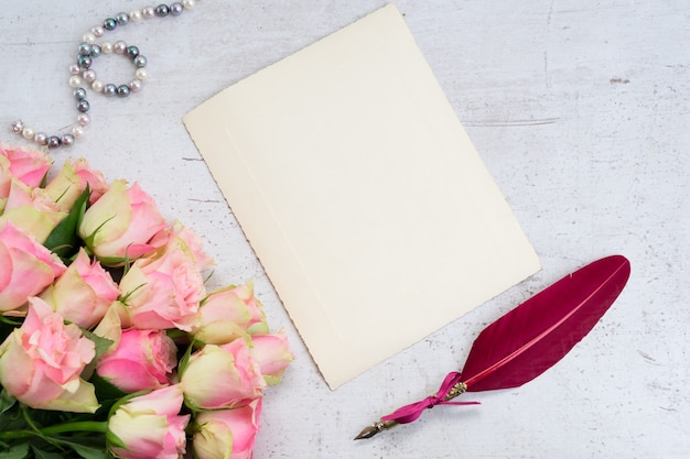 Bijoux en perles, roses et plumes sur table blanche