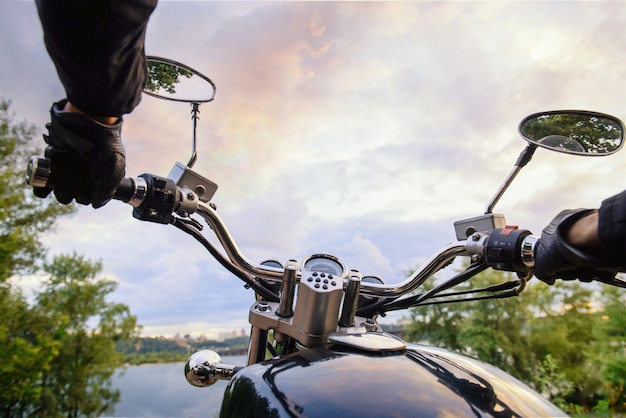 Biker conduisant une moto au coucher du soleil. Vue à la première personne sur le guidon et beau paysage