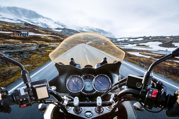 Biker conduit une moto sur une route glissante à travers un col de montagne en Norvège. Autour du brouillard et de la neige. Vue à la première personne.