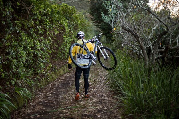 Biker homme transportant un vélo de montagne et marchant sur un chemin de terre