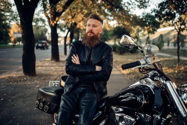 Biker en veste de cuir pose avec son chopper