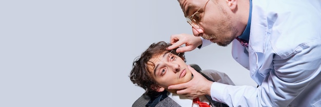 Photo bilan de santé extraordinaire médecin fou vérifiant les yeux masculins ouvrant largement les modèles contre le gris