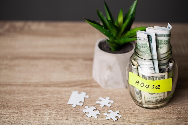 Billets d'un dollar dans un bocal en verre et une maison de texte sur une table en bois.