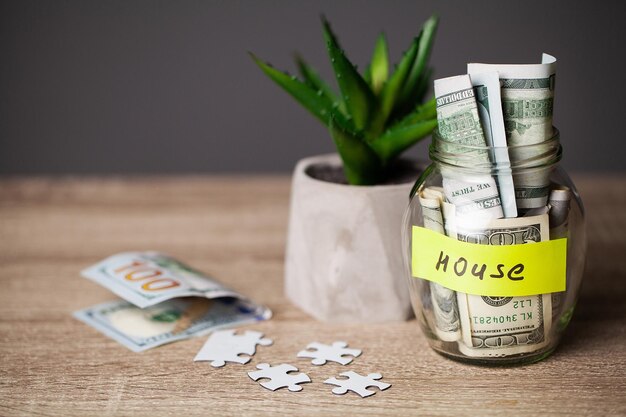 Billets d'un dollar dans un bocal en verre et une maison de texte sur une table en bois.