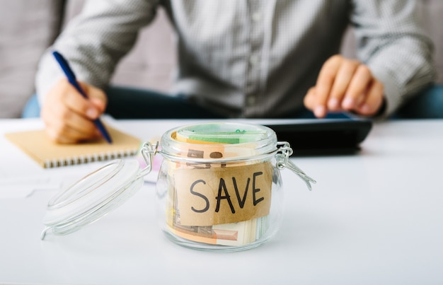 Billets en euros dans une bouteille en verre pour économiser. Homme faisant sa comptabilité. Petite entreprise : dépôt et prêt, réduction des taux d'intérêt.