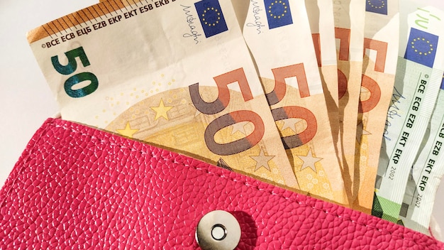 Billets en papier euro Monnaie européenne sur fond blanc gros plan Un sac à main ou un sac à main de couleur rose vif avec un bouton en métal à partir duquel l'argent est étalé Billets de 5 10 20 50 et 100