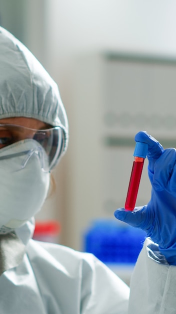 Biochimiste en combinaison tenant un échantillon de sang analysant la réaction chimique travaillant dans un laboratoire médical. Scientifique examinant l'évolution du vaccin à l'aide de la haute technologie pour le développement d'un traitement contre le virus covid19