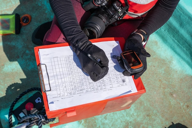 Biologiste marin méconnaissable écrivant des données sur papier sur un bateau