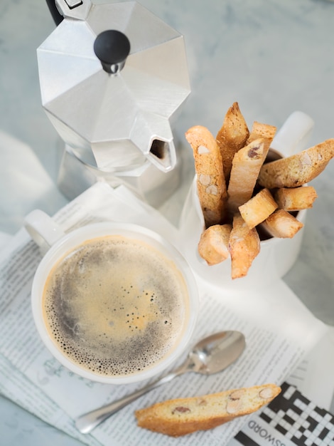 Biscotti, dessert italien traditionnel aux amandes avec une tasse de café et une cafetière Moka sur un journal.