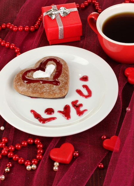 Biscuit au chocolat en forme de coeur avec une tasse de café sur une nappe rose en gros plan