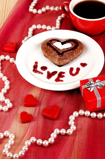 Biscuit au chocolat en forme de coeur avec une tasse de café sur une nappe rose en gros plan