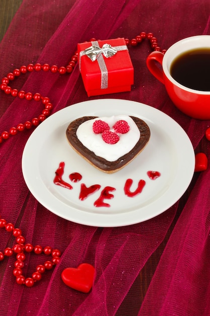 Biscuit au chocolat en forme de coeur avec une tasse de café sur une nappe rose en gros plan