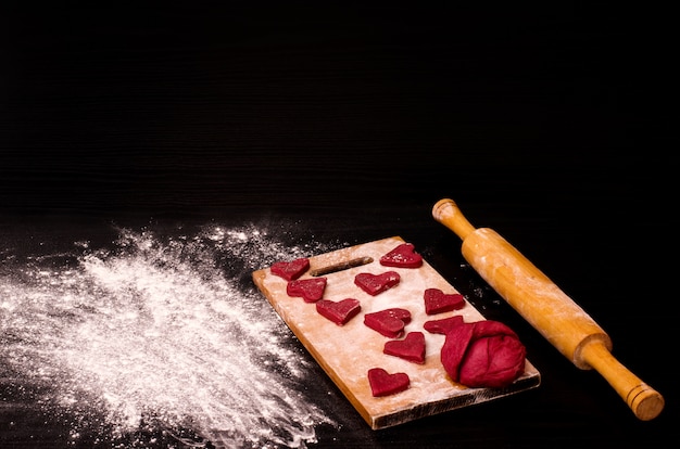 Photo biscuit coeur rouge et un morceau de pâte sur la planche de bois