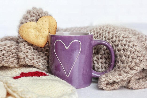 Biscuit en forme de coeur sur une tasse de café avec gros plan de tissu tricoté