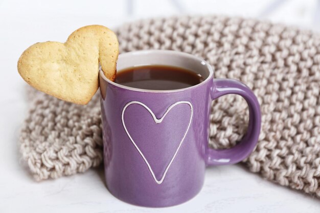 Biscuit en forme de coeur sur une tasse de café avec gros plan de tissu tricoté