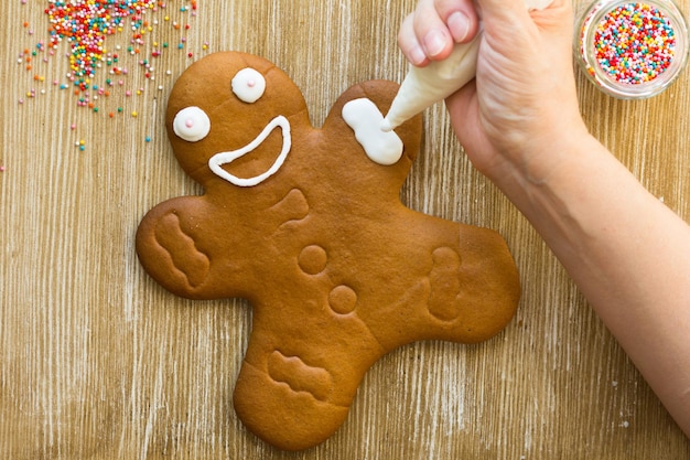 Biscuit de pain d'épice au four décoré de glaçage par une main de femme sur fond de bois