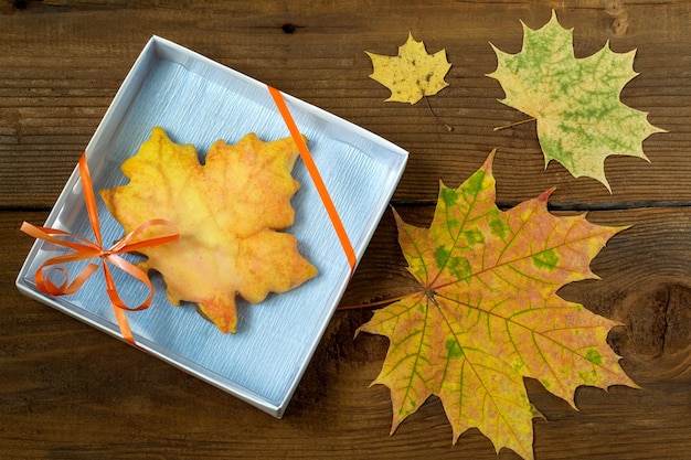 Biscuit de pain d'épice fait maison en forme de feuille d'érable dans une boîte-cadeau et des feuilles d'automne colorées