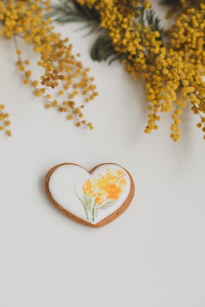 biscuit de pain d'épice en forme de coeur et fleurs de mimosa sur fond blanc. espace copie vue de dessus