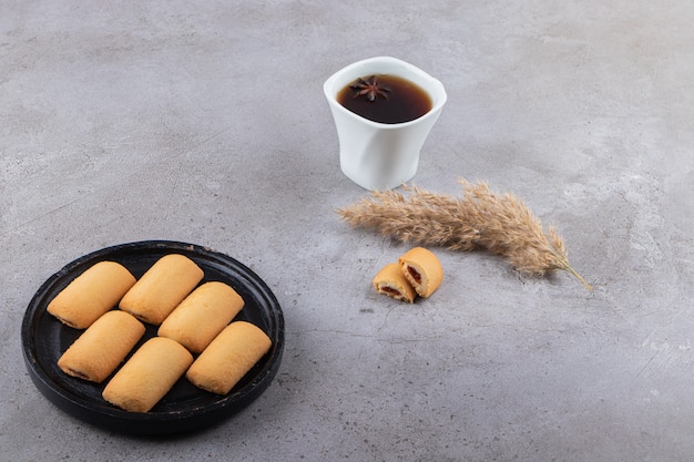 Biscuit sucré avec une tasse de thé noir placé sur une table en pierre.