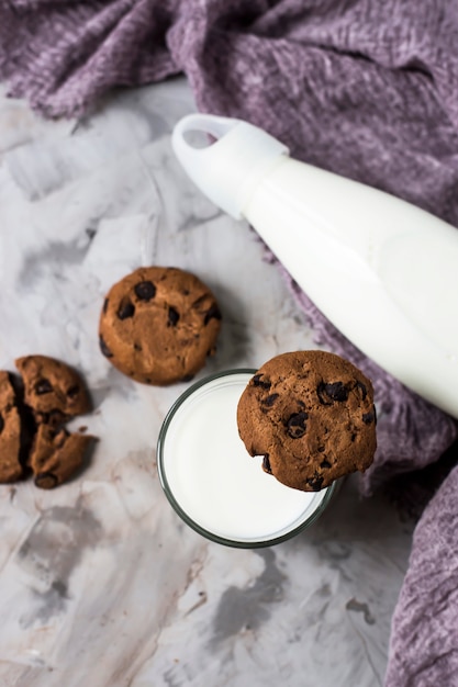 Biscuits au chocolat à côté d&#39;une bouteille en verre et un verre de lait sur une table grise