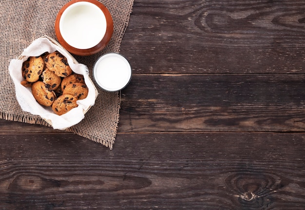 Biscuits au chocolat et lait en verre et pot sur toile de jute sur une table en bois. Mise à plat.