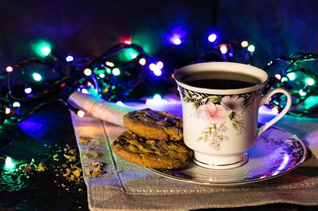 Photo biscuits au chocolat et une tasse de thé sur fond sombre avec des lumières colorées.