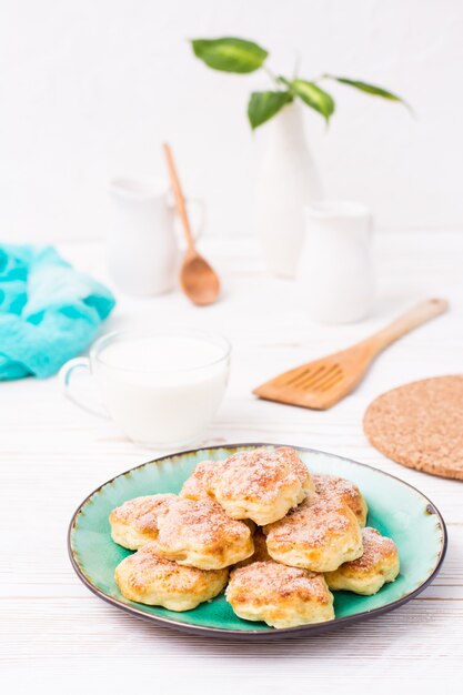 Biscuits au fromage cottage saupoudrés de sucre sur une assiette et une tasse de lait sur une table en bois