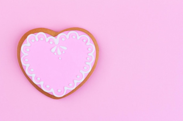 Biscuits au gingembre faits maison en forme de coeur avec glaçage rose sur fond rose avec espace de copie