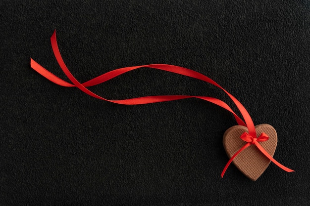 Biscuits au gingembre en forme de coeurs avec ruban rouge sur fond noir.