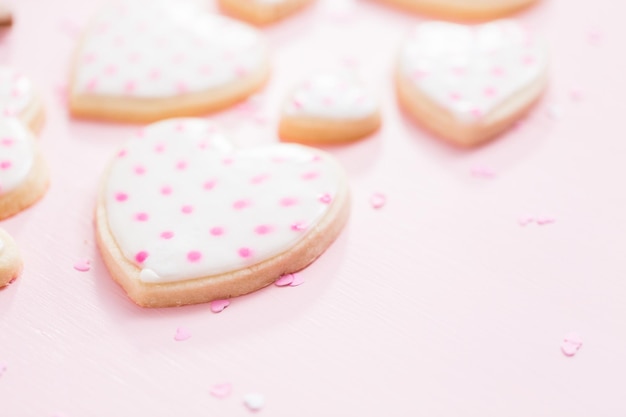 Biscuits au sucre en forme de coeur décorés de glace royale pour la Saint-Valentin sur fond rose.