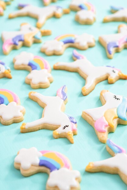 Biscuits au sucre de licorne décorés de glaçage royal et de paillettes alimentaires sur fond bleu.