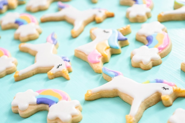 Biscuits au sucre de licorne décorés de glaçage royal et de paillettes alimentaires sur fond bleu.