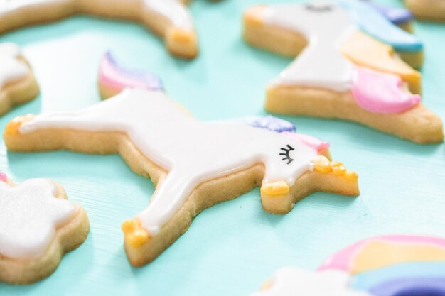 Biscuits au sucre de licorne décorés de glaçage royal et de paillettes alimentaires sur fond bleu.