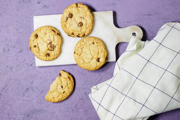 biscuits aux pépites de chocolat faits maison dans une planche à découper en marbre sur fond grunge violet