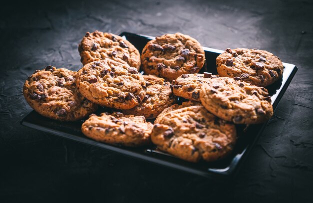 Biscuits aux pépites de chocolat maison sur une plaque carrée noire sur une table sombre