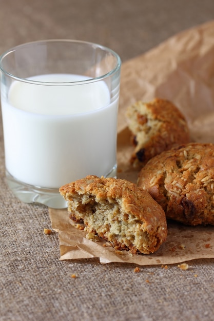 Biscuits à l'avoine cassés avec des chats et verre avec du lait sur du papier d'emballage kraft et nappe de jute.