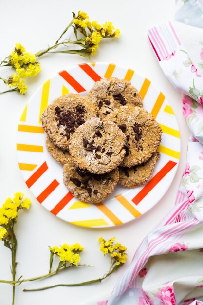 Biscuits à l'avoine avec du chocolat sur une assiette avec un tissu brillant et des fleurs