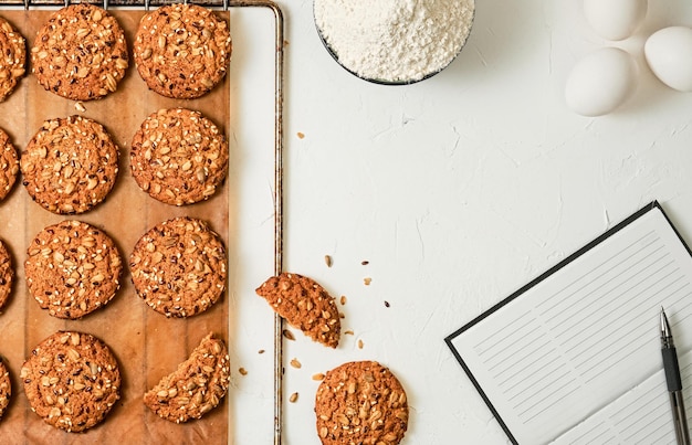 Biscuits à l'avoine faits maison avec graines de lin et de sésame sur une plaque à pâtisserie, fond blanc avec espace de copie. Oeufs, farine - ingrédients pour faire des biscuits, disposition de la table. Pâtisseries maison pour les fêtes